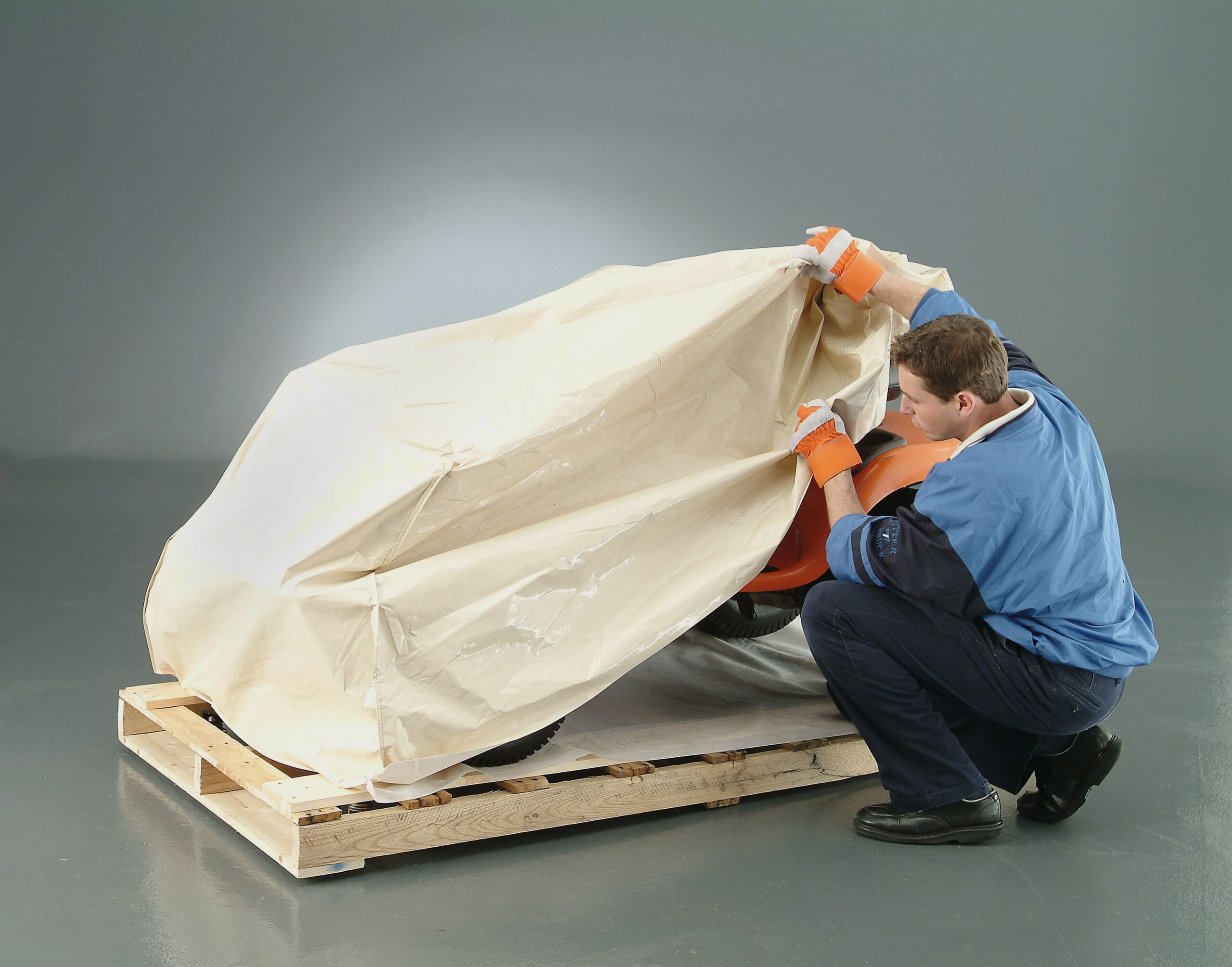 Man Covering a Tractor on a Pallet with a Cover