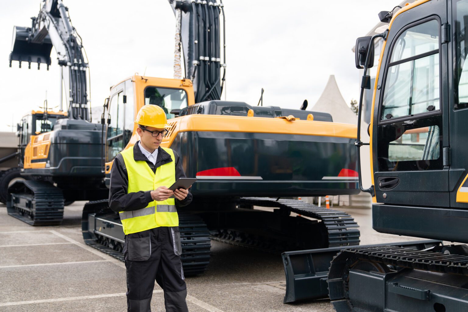 Engineer in a helmet with a digital tablet inspects construction excavators